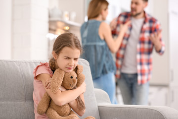 Wall Mural - Little unhappy girl sitting on sofa while parents arguing at home