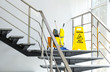 © New Africa - Safety sign with phrase Caution wet floor and mop bucket on stairs. Cleaning service