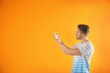 Poster - Young man with air conditioner remote on color background