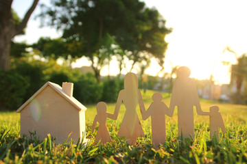 Wall Mural - image of happy family concept. wooden cut people holding hands together next to home in green grass during sunset.