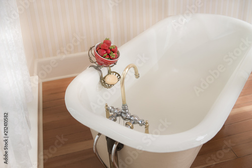 Fotografie, Obraz Antique bathtub with soap and strawberries in brass hanger on the edge