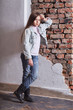 Fashion little girl standing leaning brick wall. Stylish model kid. Young caucasian child in casual stylish clothes, denim jacket, white singlet cotton, youth jeans. High fashion urban style.