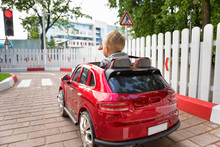 Little Smiling Boy Is Driving A Car On Kid's Go-karting. Three Year-old Child In A Red Toy Car In The Children's Race Track With Road Signs And Traffic Light Having Fun Outdoors, Attention Concept