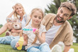 © LIGHTFIELD STUDIOS - mother with teddy bear looking at happy father and daughter blowing soap bubbles in park