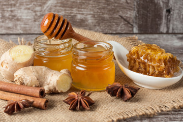 Honey dripping from a wooden honey dipper in a jar on wooden grey rustic background