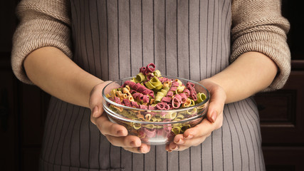 Wall Mural - Womal holding glass bowl with dried colourful pasta