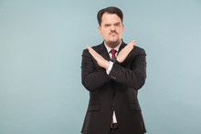 Man Showing X Sign Of Hands. Bad Sign. Do Not Even Try To Convince Me To Do This.. Indoor Studio Shot. Isolated On Light Blue Background. Handsome Businessman With Black Suit, Red Tie And Mustache.