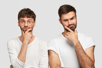 Wall Mural - Indoor shot of two young bearded men hold chins and look seriously at camera, ponder about making project work, want to achieve success, isolated over white background. Collaboration concept