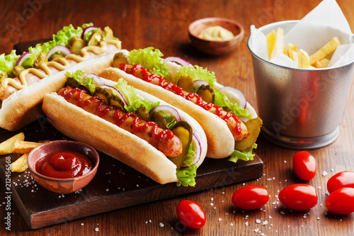 Fotografie, Obraz Hot dog with grilled sausage, ketchup, mustard and fries on wooden kitchen board
