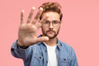© wayhome.studio  - Serious handsome bearded hipster stretches hand towards camera, shows palm, demonstrates stop or hold gesture, wears fashionable clothes, stands against pink background. Stay away from me, please