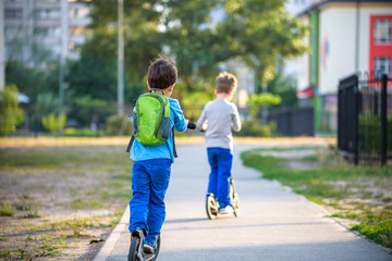 Wall Mural - Two cute boys, compete in riding scooters, outdoor in the park, summertime. Kids are happy playing outdoors. Two brothers standing on their scooters