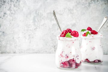 Healthy breakfast, cream dessert, frozen yogurt with fresh raspberries, raspberry jam, served with fresh mint leaves. On light concrete background, copy space