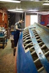 Wall Mural - Young man in workwear standing by unfinished ship construction and working over it