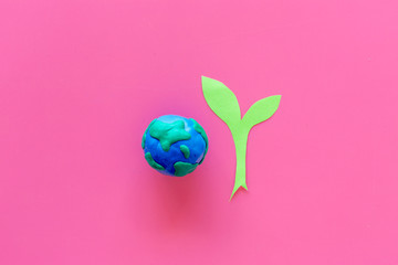 Planet, ecology. plastiline symbol of planet Earth globe and plant coutout on pink background top view copy space