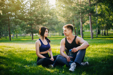 A young girl and a guy are sitting on the grass and talking. Doing sports outdoors. People in sportswear do gymnastics. Rest after sports