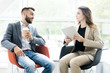 © Seventyfour - Portrait of two modern business people, man and woman, sitting in designer chairs and talking to each other in sunlit room