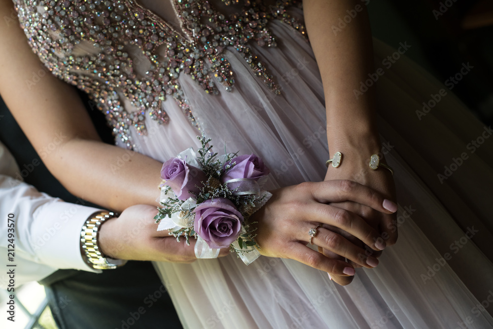 Close up of prom or weeding couple, focusing on an elegant girl's hands, with a diamond ring and crystal bracelet. Woman is wearing a purple dress with crystal beads, and a purple rose corsage. - obrazy, fototapety, plakaty 