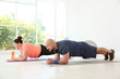 © New Africa - Overweight man and woman doing plank exercise on mats in gym