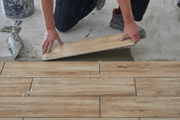 Hands of the tiler are laying the ceramic wood effect tiles on the floor