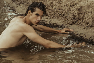 Strong face sport sexy male model on the sea shore background with sand and water on the beach on the sunset