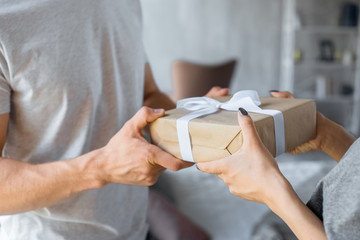 partial view of man presenting wrapped gift to girlfriend at home