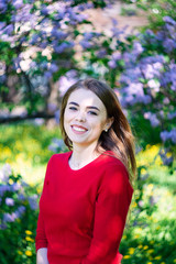 Wall Mural - Beautiful young woman in a red sweater in the park near the lilac blossom.