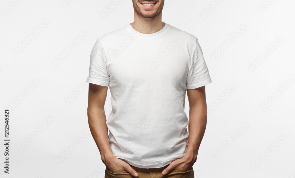 Handsome man in white tshirt isolated on grey background, smiling, standing in hands in pockets pose - obrazy, fototapety, plakaty 