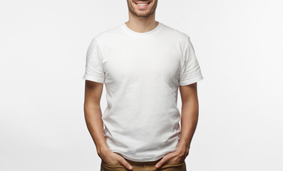 handsome man in white tshirt isolated on grey background, smiling, standing in hands in pockets pose