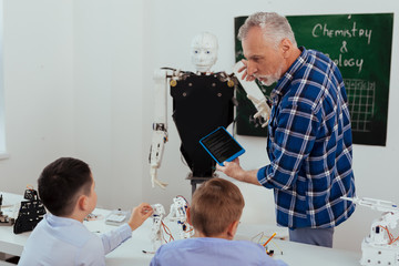 Wall Mural - this is future. smart professional teacher pointing at the robot while talking to his pupils