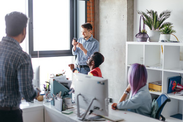 Wall Mural - Teamwork in action. Handsome young Indian man in casual wear explaining his point of view while his colleagues listening to him attentively