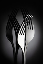 Two Interlocking Shiny Forks On Reflective Black Background For Artistic Minimalist Still Life. Shadowy Reflection.