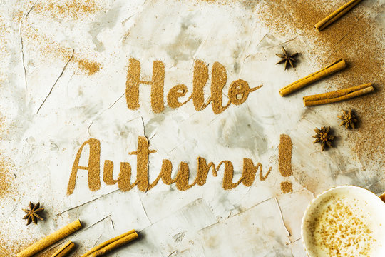 Hello, Autumn. The phrase is written on a gray table with ground cinnamon among cinnamon sticks and badyan. Top view, flat lay