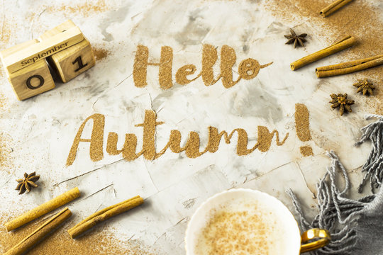 Hello, Autumn. The phrase is written with ground cinnamon on a gray background. Next to the wooden calendar on which the date is September 1. Top view, flat lay