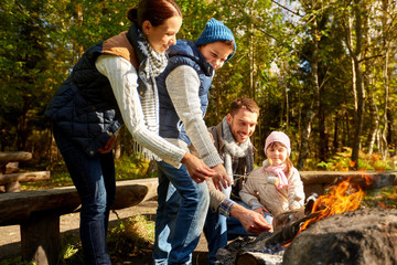 Canvas Print - camping, travel, tourism, hike and people concept - happy family roasting marshmallow over campfire