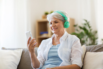 Wall Mural - technology, people and lifestyle concept - happy senior woman in headphones and smartphone listening to music at home