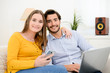 © W PRODUCTION - cheerful young couple on sofa at home websurfing and shopping online with laptop computer internet technology