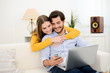 © W PRODUCTION - cheerful young couple on sofa at home websurfing and shopping online with laptop computer internet technology
