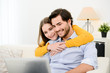 © W PRODUCTION - cheerful young couple on sofa at home websurfing and shopping online with laptop computer internet technology
