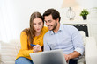 © W PRODUCTION - cheerful young couple on sofa at home websurfing and shopping online with credit card, a laptop computer and internet technology