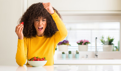 Poster - African american woman eating strawberries at home annoyed and frustrated shouting with anger, crazy and yelling with raised hand, anger concept