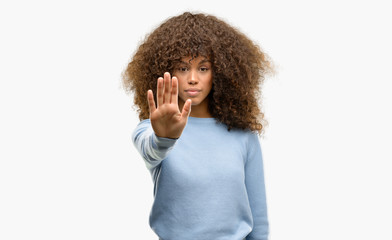 Canvas Print - African american woman wearing a sweater doing stop sing with palm of the hand. Warning expression with negative and serious gesture on the face.