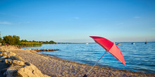 Parasol At Sunset At Lake Garda In Italy, Gravel Beach At City Of Bardolino