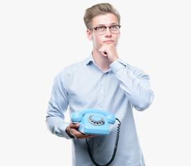 Sticker - Young handsome blond man holding vintage telephone serious face thinking about question, very confused idea