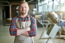Waist Up Portrait Of Smiling Bearded Man Wearing Apron Posing Standing Confidently With Arms Crossed Against Roasting Machines In Artisan Coffee Roastery, Copy Space