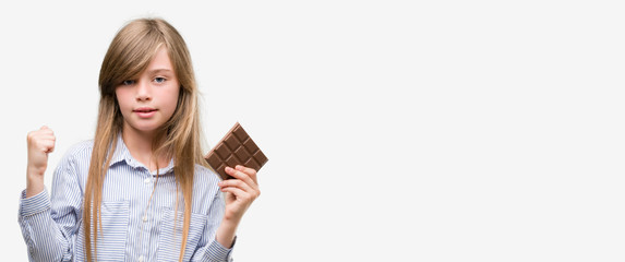 Sticker - Young blonde child holding chocolate bar screaming proud and celebrating victory and success very excited, cheering emotion