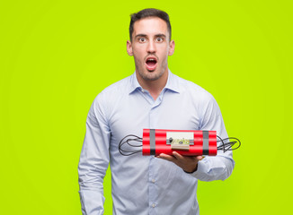 Canvas Print - Handsome young business man holding an alarm clock bomb scared in shock with a surprise face, afraid and excited with fear expression