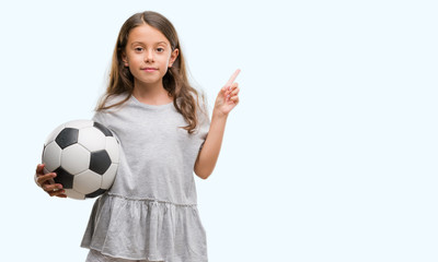 Poster - brunette hispanic girl holding soccer football ball very happy pointing with hand and finger to the 