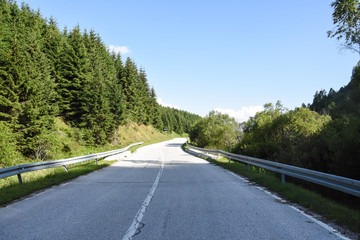 Mountain road. Old road through the forest. Concept of travel under a blue sky