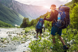 Fototapeta Las - Tourists with hiking backpacks on beautiful mountain landscape background. Climbers hike to mounts. Group of hikers walking in mountains