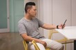 © Wavebreak Media - Young man using smartphone while sitting on chair
